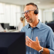 Kaufland-Mitarbeiter mit Headset vor einem Bildschirm in angeregtem Gespräch bei einer Telko.
